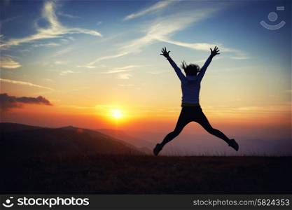 Silhouette of young woman jumping against sunset with blue sky.