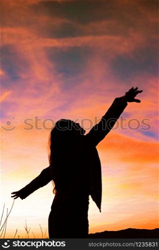 Silhouette of young woman with open arms against colorful sky