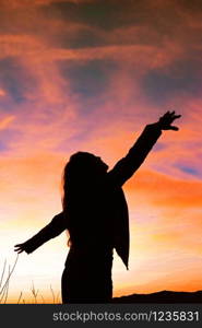 Silhouette of young woman with open arms against colorful sky