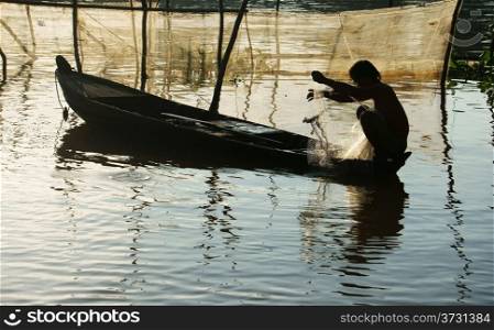 silhouette &rsquo;s fisherman sitting on row boat, pick up the net, repair for fishing to catch fish on river at morning in flood season