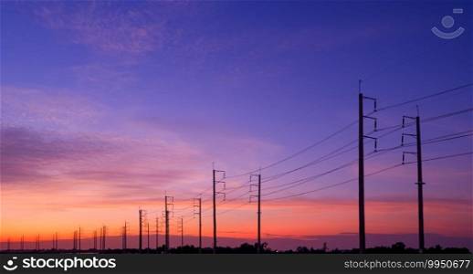 Silhouette two rows of electric poles with cable lines in countryside area against colorful dramatic sunset sky background in panoramic view