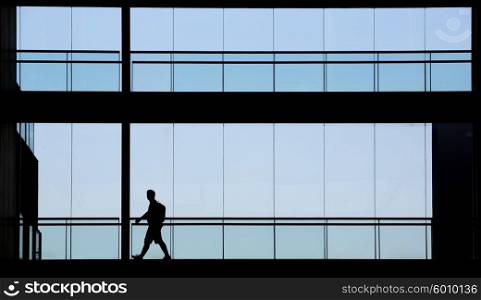 Silhouette view of young businessman walking in modern office building interior with panoramic windows.
