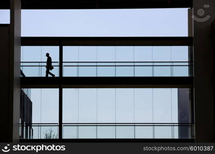 Silhouette view of young businessman walking in modern office building interior with panoramic windows.