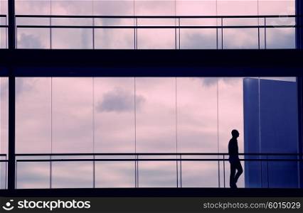 Silhouette view of young businessman walking in modern office building interior with panoramic windows.