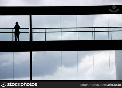 Silhouette view of young businesswoman in a modern office building interior with panoramic windows.