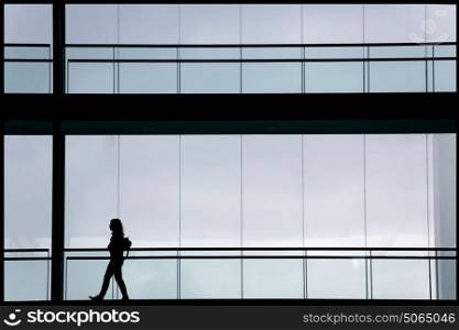 Silhouette view of young businesswoman in a modern office building interior with panoramic windows.