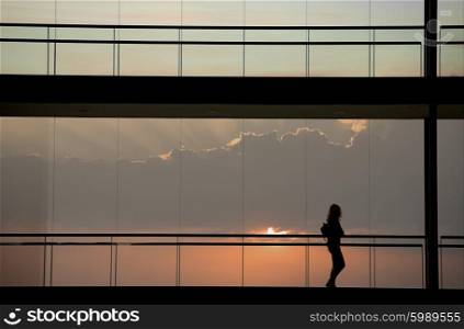 Silhouette view of young businesswoman walking in modern office building interior with panoramic windows.