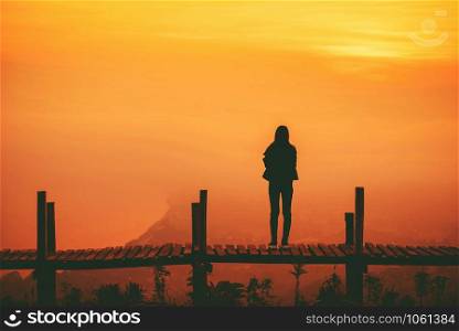Silhouette woman standing on wooden bridge on hill mountain and sunset yellow sky background