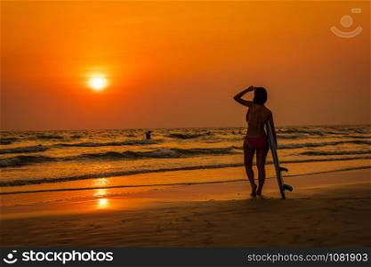 silhouette young asian women tourist in bikini with holding hands surfboard on the beach and the sunset seascape background travelling summer holiday concept