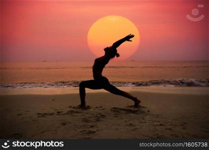 Silhouette young woman practicing yoga on the beach at sunrise