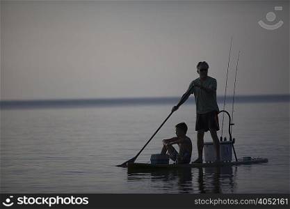 Silhouetted man and teenage son fishing from paddleboard in Lake Superior, Au Train Bay, Michigan, USA