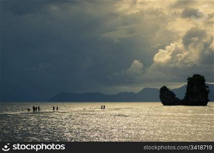 Silhouetted people seemingly walking on water leading to an island