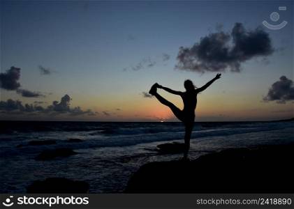Silhouetted to hold bind balance pose at sunrise along the coast.