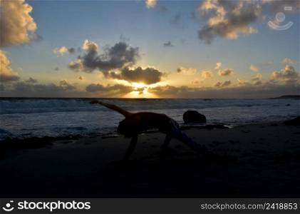 Silhouetted yoga flipped dog pose at sunrise along the coast.