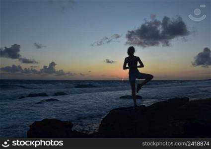 Silhouetted yoga tree pose at sunrise on the coast of Aruba.