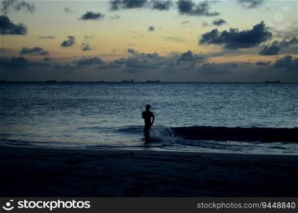 Silhouetted young man running into the water along the coast of Aruba.