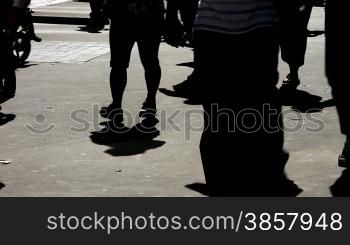 Silhouettes and shadows of people walking on the bright pavement of an urban sidewalk