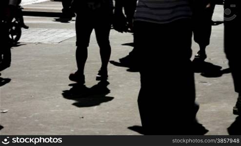 Silhouettes and shadows of people walking on the bright pavement of an urban sidewalk