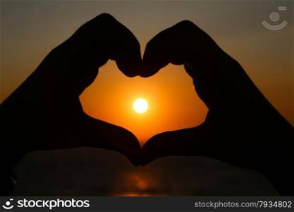 Silhouettes hand heart shaped with sun sets and the sky orange