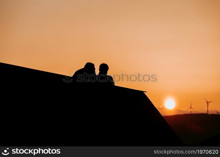 Silhouettes of a couple in a balcony looking the sunset in the mountains