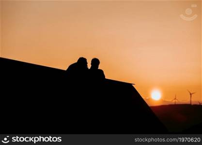 Silhouettes of a couple in a balcony looking the sunset in the mountains