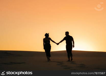 silhouettes of a happy young couple guy and girl on a background of orange sunset in the sand desert