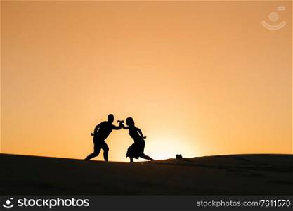 silhouettes of a happy young couple guy and girl on a background of orange sunset in the sand desert