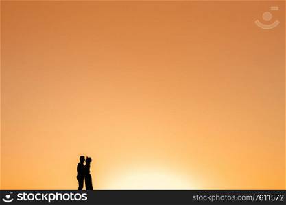 silhouettes of a happy young couple guy and girl on a background of orange sunset in the sand desert