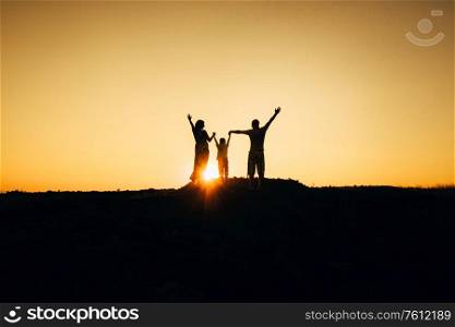silhouettes of a happy young happy family against an orange sunset in the desert