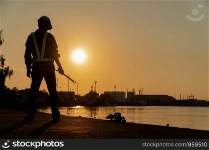 Silhouettes of asian man engineer holding wrenches and standing on shipyard and background is oil storage silo.
