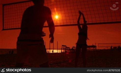 Silhouettes of beach volleyball players at sunset