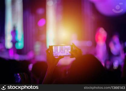 silhouettes of concert crowd at Rear view of festival crowd raising their hands and using smartphone take photo and video on bright stage lights