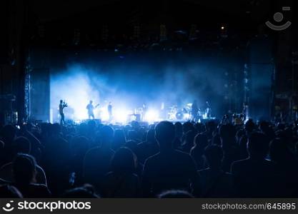 Silhouettes of crowd, group of people, cheering in live music concert in front of colorful stage lights.