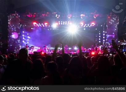 Silhouettes of crowd, group of people, cheering in live music concert in front of colorful stage lights.