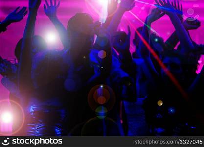 Silhouettes of dancing people having a celebration in a disco club, the light show is sending laser beams through the backlit scene