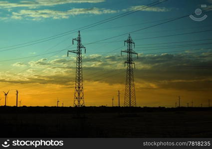 Silhouettes of electricity pillars and wind turbines on sunset