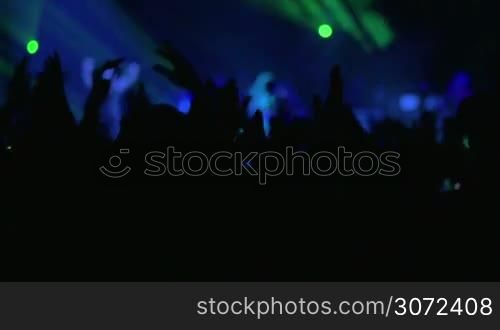 Silhouettes of excited fans giving applause to the musician performing on the stage with colorful lighting effects