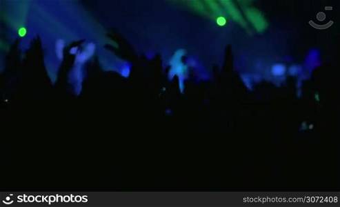 Silhouettes of excited fans giving applause to the musician performing on the stage with colorful lighting effects
