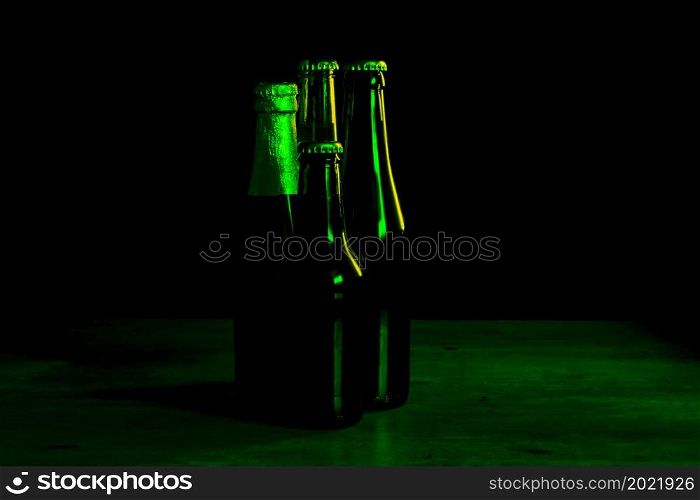 silhouettes of four beer bottles on a black background with green lights that illuminate them on one side.. silhouettes of four beer bottles on a black background with green lights that illuminate them on one side