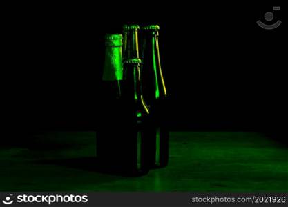 silhouettes of four beer bottles on a black background with green lights that illuminate them on one side.. silhouettes of four beer bottles on a black background with green lights that illuminate them on one side