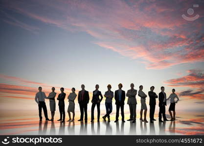 Silhouettes of group of business people standing in line on sunset background . They are proffesionals