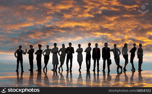 Silhouettes of group of business people standing in line on sunset background . They are proffesionals