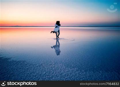 Silhouettes of hugging happy lovers in middle of shallow water of lake at sunset. The concept of love, happiness, family, solitude. Salt Lake Tuz, Turkey. Silhouettes of hugging happy lovers in middle of shallow water of lake at sunset