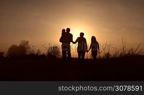 Silhouettes of loving grandparents with two kids walking in the meadow in glowing of amazing sunset in springtime. Multi generation family with siblings enjoying great time in setting sun. Slow motion. Steadicam stabilized shot.