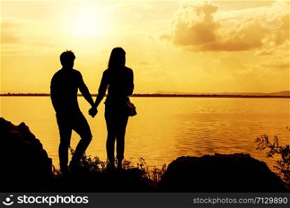 Silhouettes of man and woman holding hands while at sunset