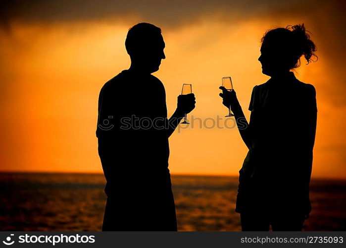 Silhouettes of man and woman with glasses on sea sunset