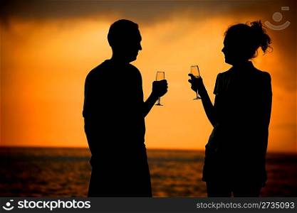 Silhouettes of man and woman with glasses on sea sunset