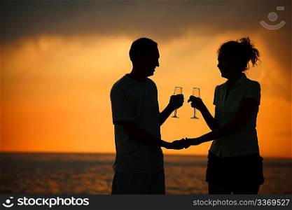 Silhouettes of man and woman with glasses on sea sunset