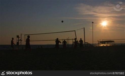 Silhouettes of men and women playing beach volleyball