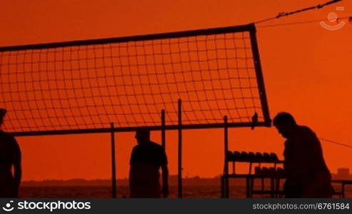 Silhouettes of men and women playing beach volleyball